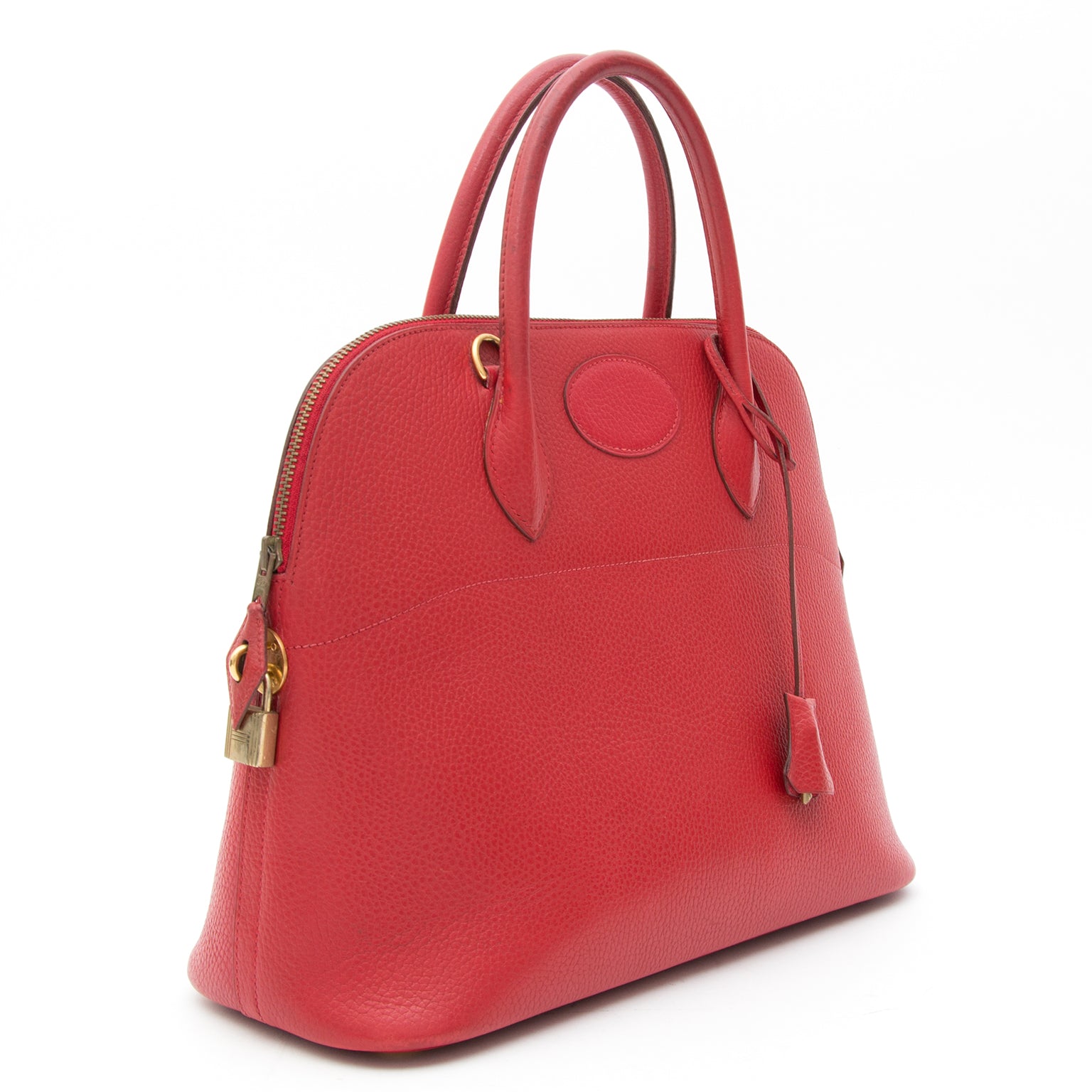 This Hermès Bolide is a classic top handle bag in tomato red Veau Grainé leather. Gold-tone padlock and hardware. Complete with clochet cadenas keyholder. Blindstamp 'A' in a circle.