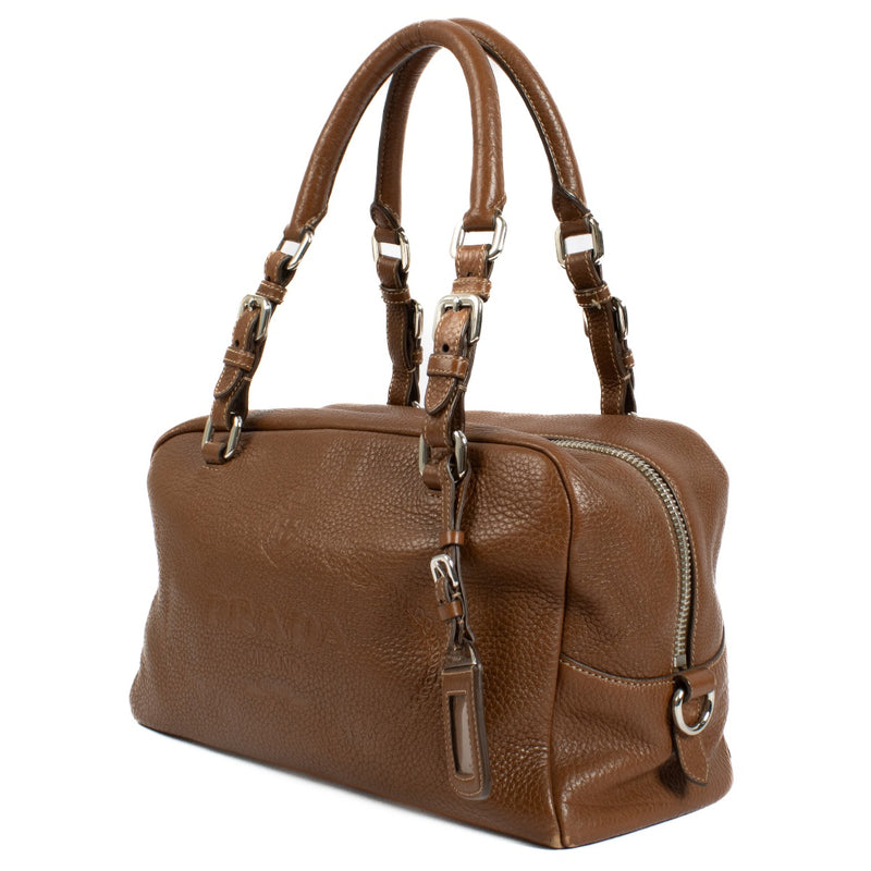Prada Brown Vitello Daino Bauletto Bag crafted from textured Vitello Daino leather, featuring a sleek structured design, gold-tone hardware, and spacious interior.Shop now on Labellov.com.