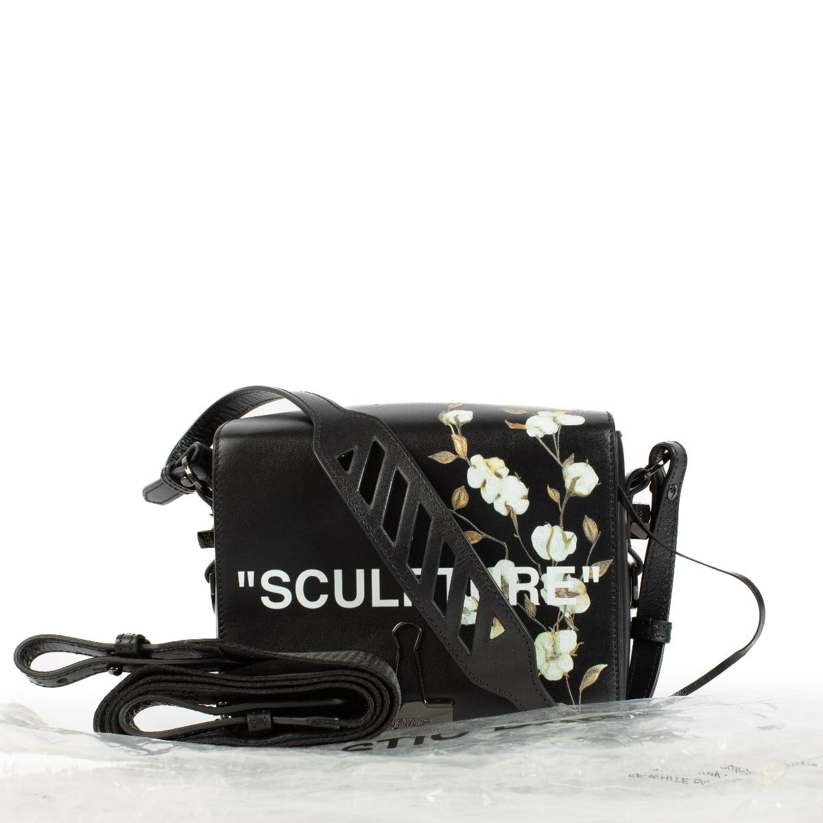 Black leather shoulder bag with cotton flower print, Off-White cut-out strap, 'SCULPTURE' text print, magnetic closure, and binder clip detail at the front. Includes one black shoulder strap. Shop now on Labellov.com.