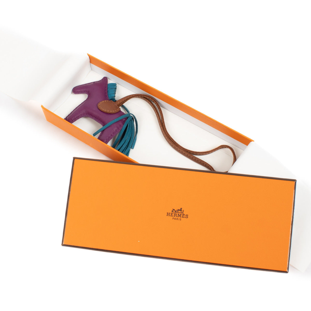 The Hermès Rodeo PM Charm brings a playful touch of luxury to any bag with its whimsical horse silhouette and vibrant colors. Crafted from soft lambskin leather, this charm features a rich purple body, a blue mane, and a brown saddle, blending elegance wi
