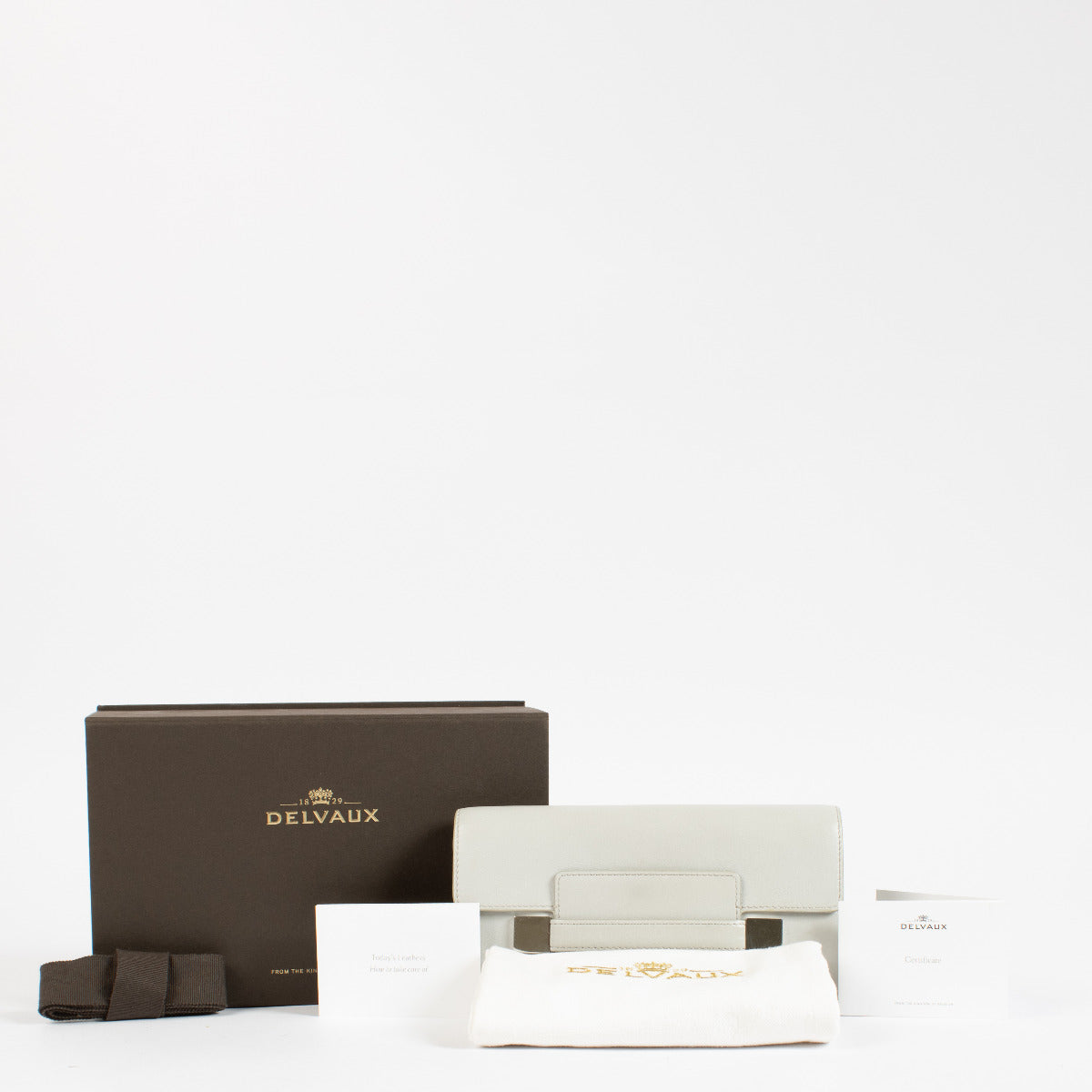 Crafted from smooth grey box calf leather, this structured wallet balances minimalist form with exceptional functionality. The sleek silhouette is accented by a distinctive rectangular flap with metallic detailing, offering a subtle yet luxurious nod to t